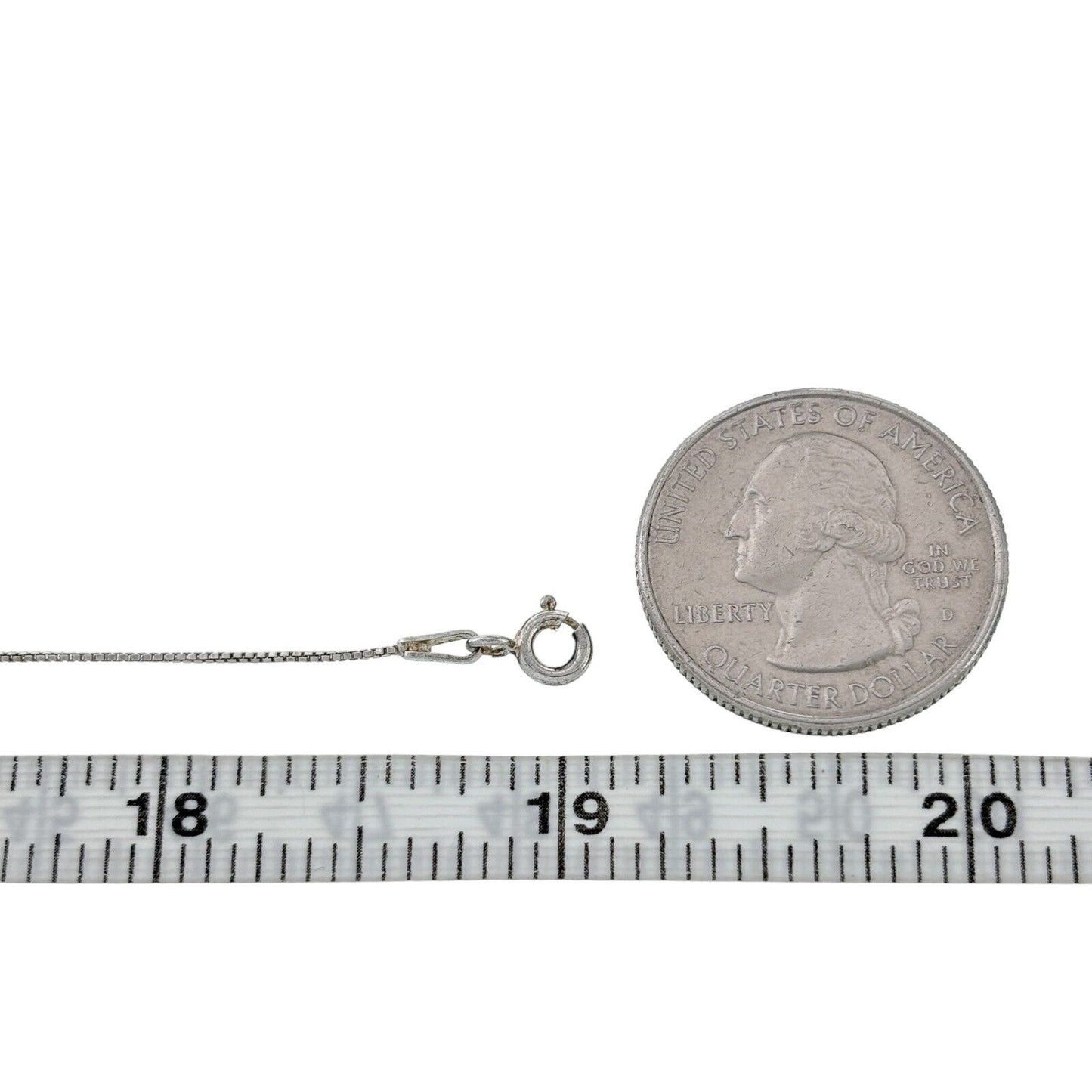 Silver necklace next to a quarter and measuring tape on a white background