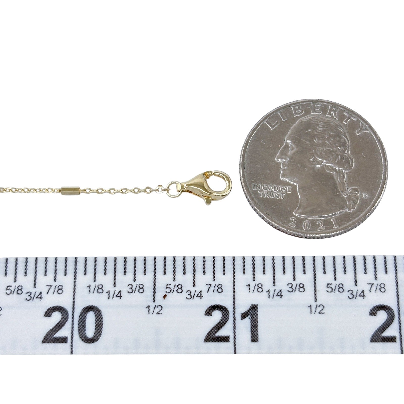 Gold necklace with clasp next to a quarter and ruler for measurement on a white background