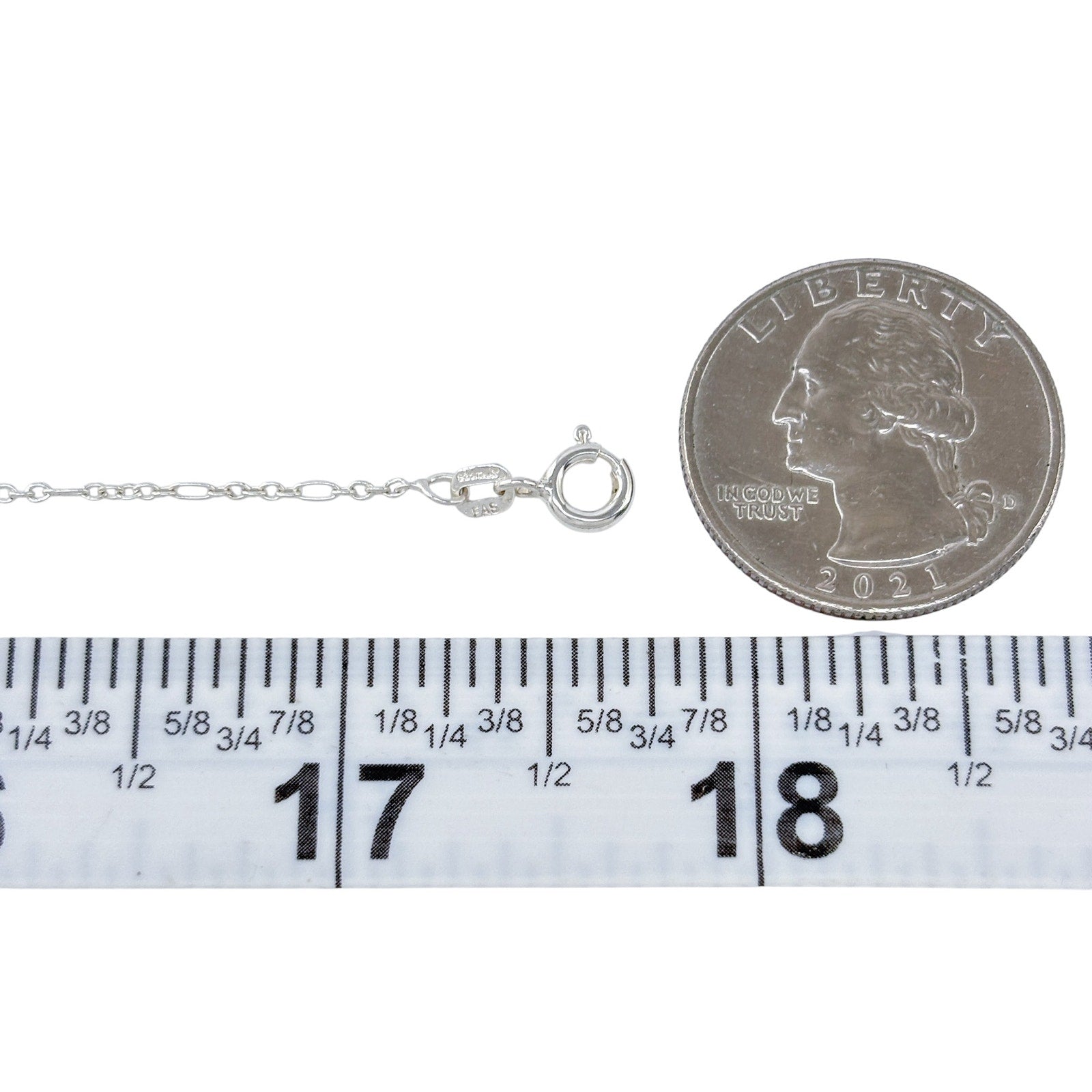 Silver bracelet next to a quarter and ruler for size reference on a white background