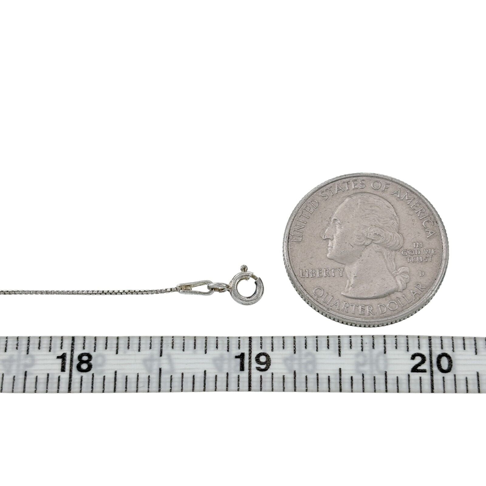Silver necklace next to a quarter and measuring tape on a white background