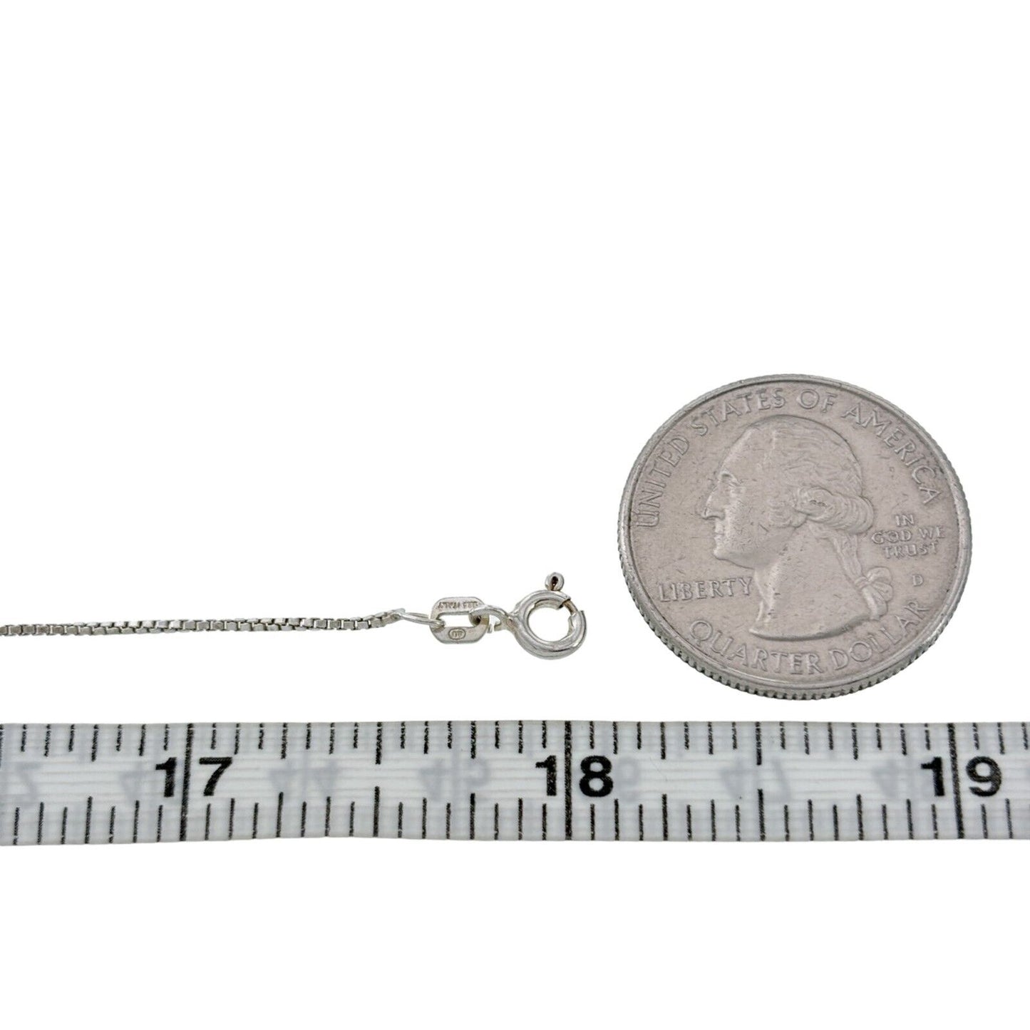 Silver necklace with clasp next to a quarter and measuring tape on a white background