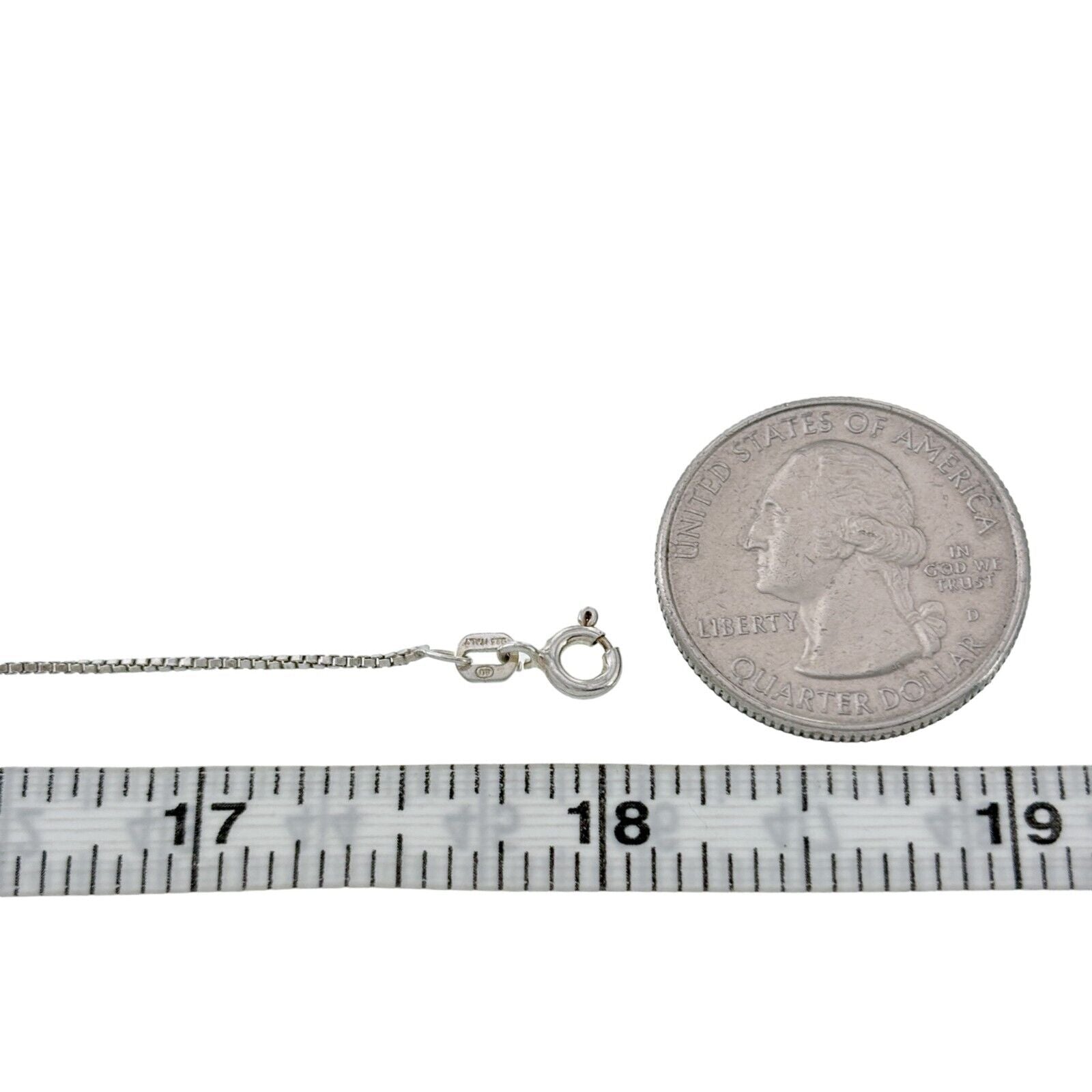Silver necklace with clasp next to a quarter and measuring tape on a white background